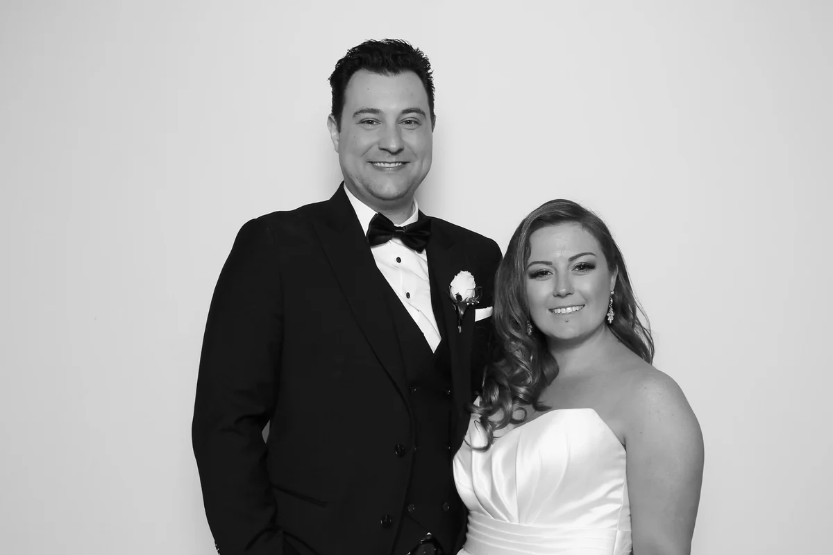Meghan and Anthony smiling together in a black-and-white photo booth portrait