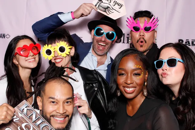 Large group wearing colourful photo booth props in front of a branded step-and-repeat backdrop.