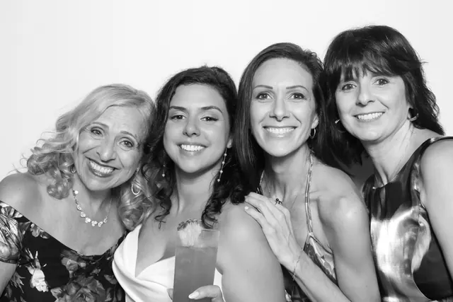 Bride smiling with three wedding guests in a black-and-white photo booth portrait.