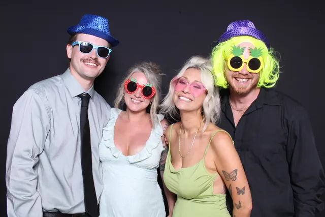 Four guests wearing bright hats, wigs and sunglasses against a black backdrop.