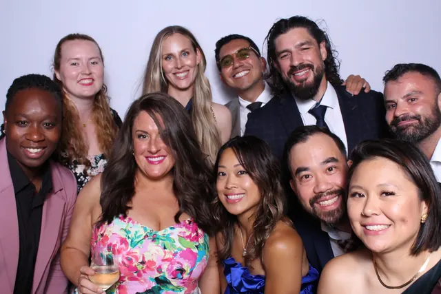 Large group of formally dressed guests smiling in an open-air photo booth.
