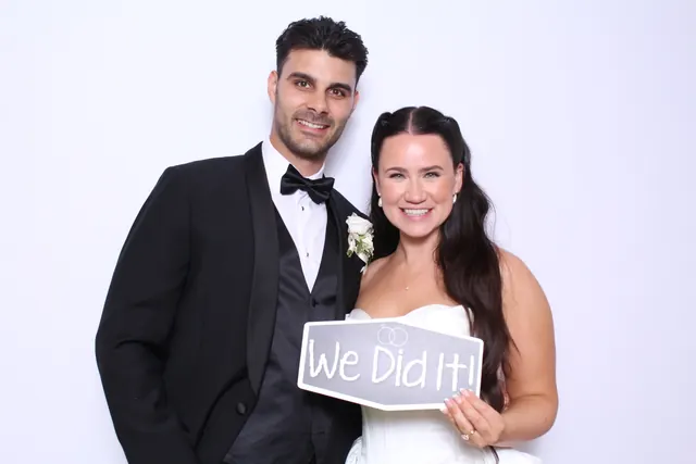 Newlyweds smiling together while holding a We Did It sign in the photo booth.