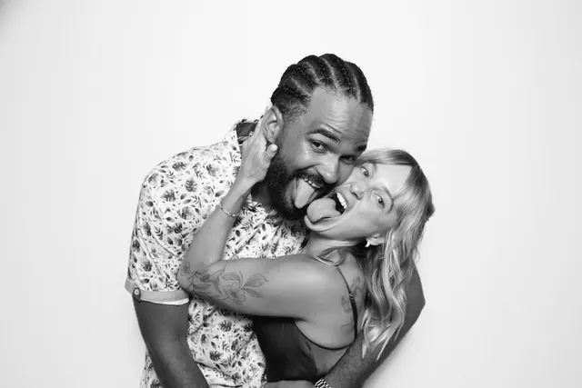 Playful couple laughing together in a black-and-white photo booth portrait.