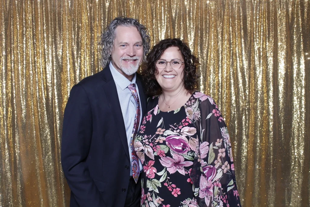 Two wedding guests smiling together in front of a gold sequin backdrop