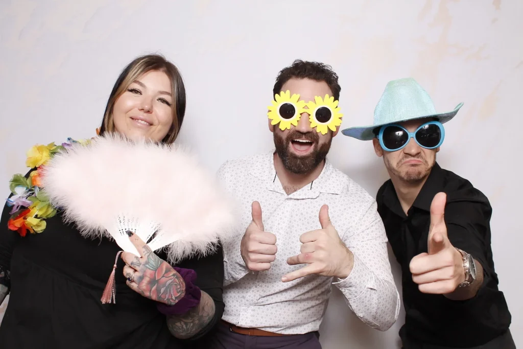 Three EPN Social guests posing with a feather fan, novelty glasses, and a hat
