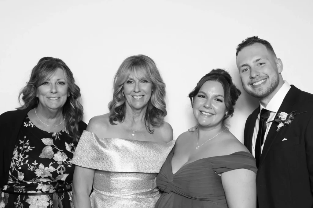 Four wedding guests smiling together against a clean white background in black and white